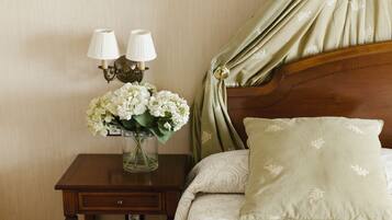 Un lit bien fait, avec un coussin à motifs et un vase de fleurs blanches posé sur une table de chevet en bois.