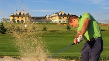 A man playing golf on a course with a large building in the background.