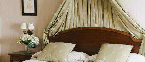 Una cama con dosel y cuatro columnas, una mesita de noche con dos lámparas y un florero con flores.