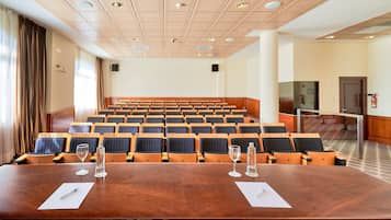 A conference room with a large wooden table, rows of chairs, and a stage area.