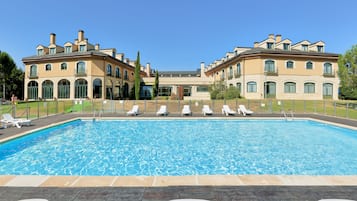 Una gran piscina con sillas de descanso y un edificio imponente con numerosas ventanas y balcones.