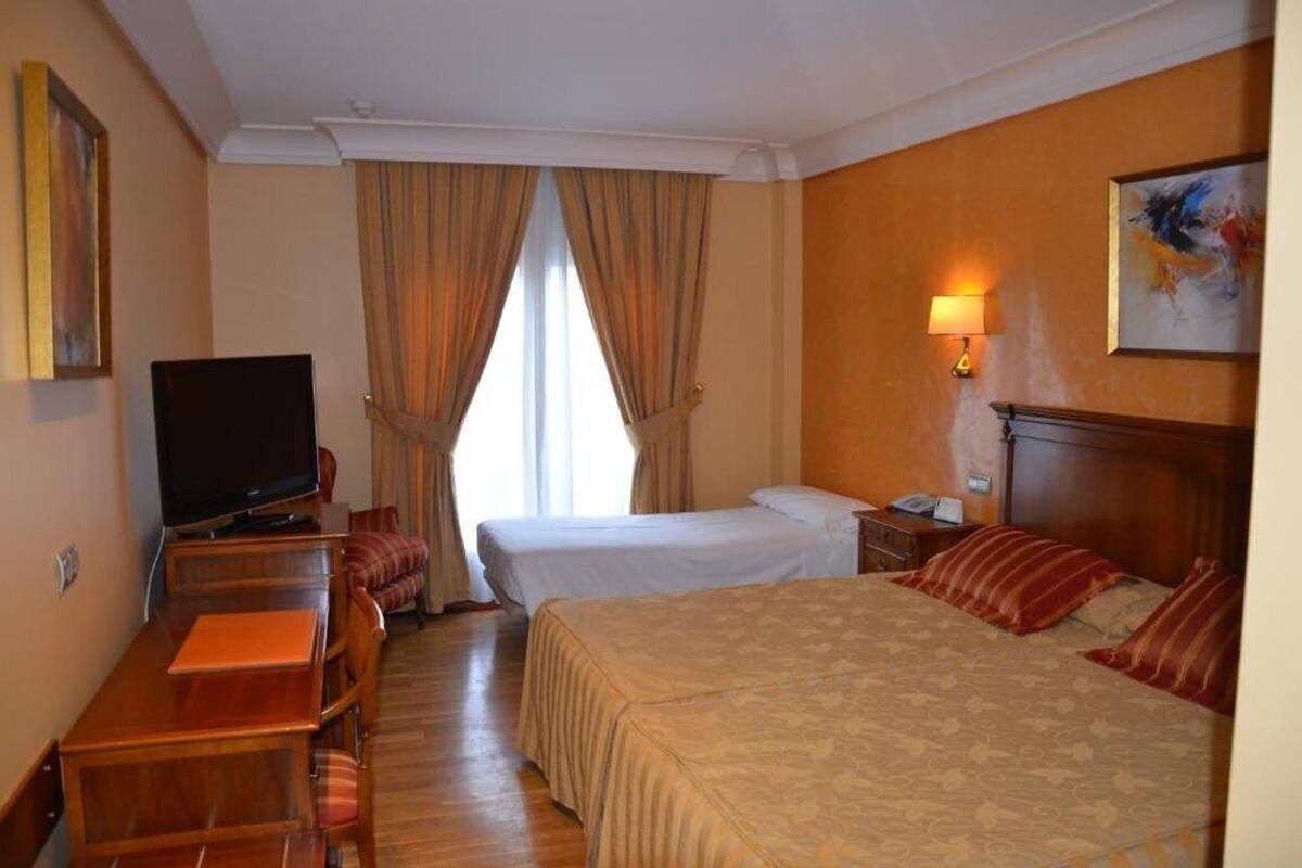 A hotel room with a bed, a desk with a television, a lamp, and a painting on the wall.