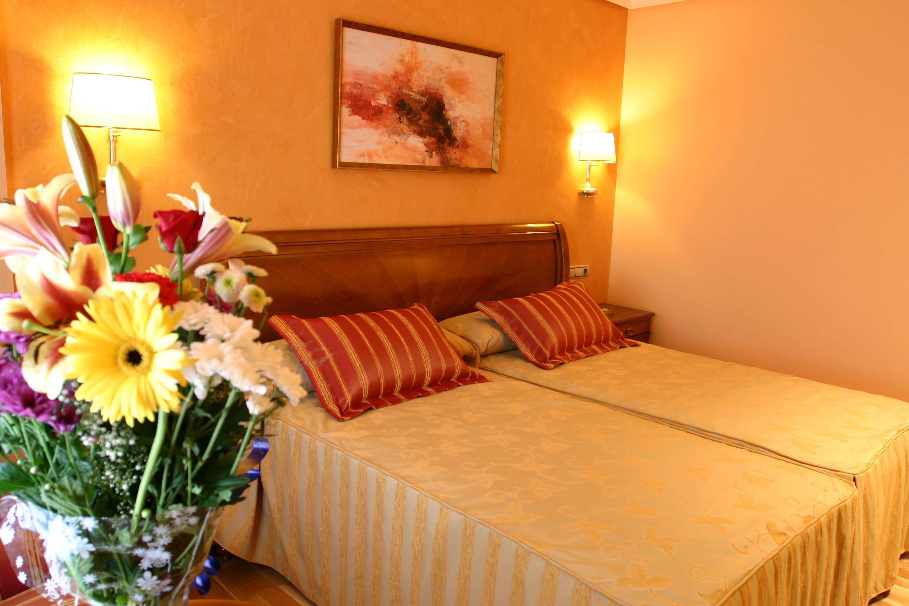 A hotel room with two beds, a floral arrangement, and wall-mounted lamps.