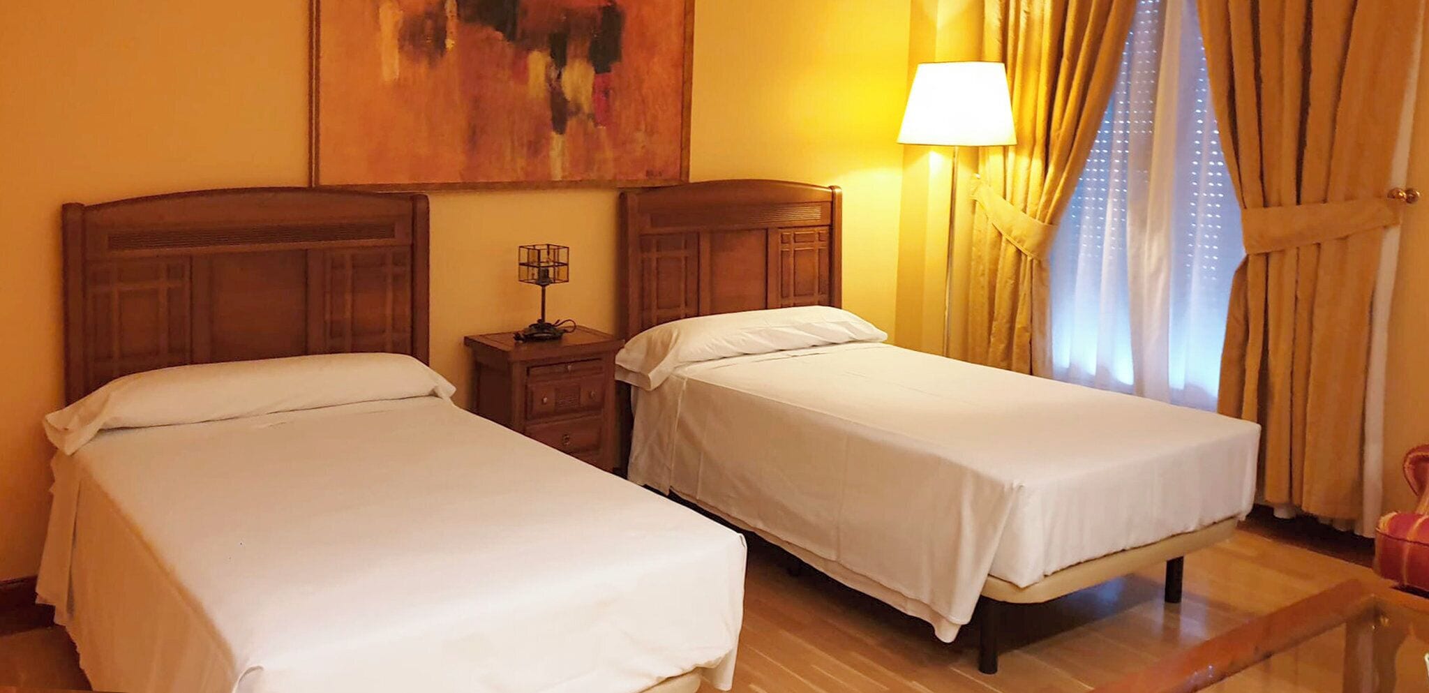 Una habitación de hotel con dos camas individuales, una mesita de noche, una lámpara y un cuadro en la pared.
