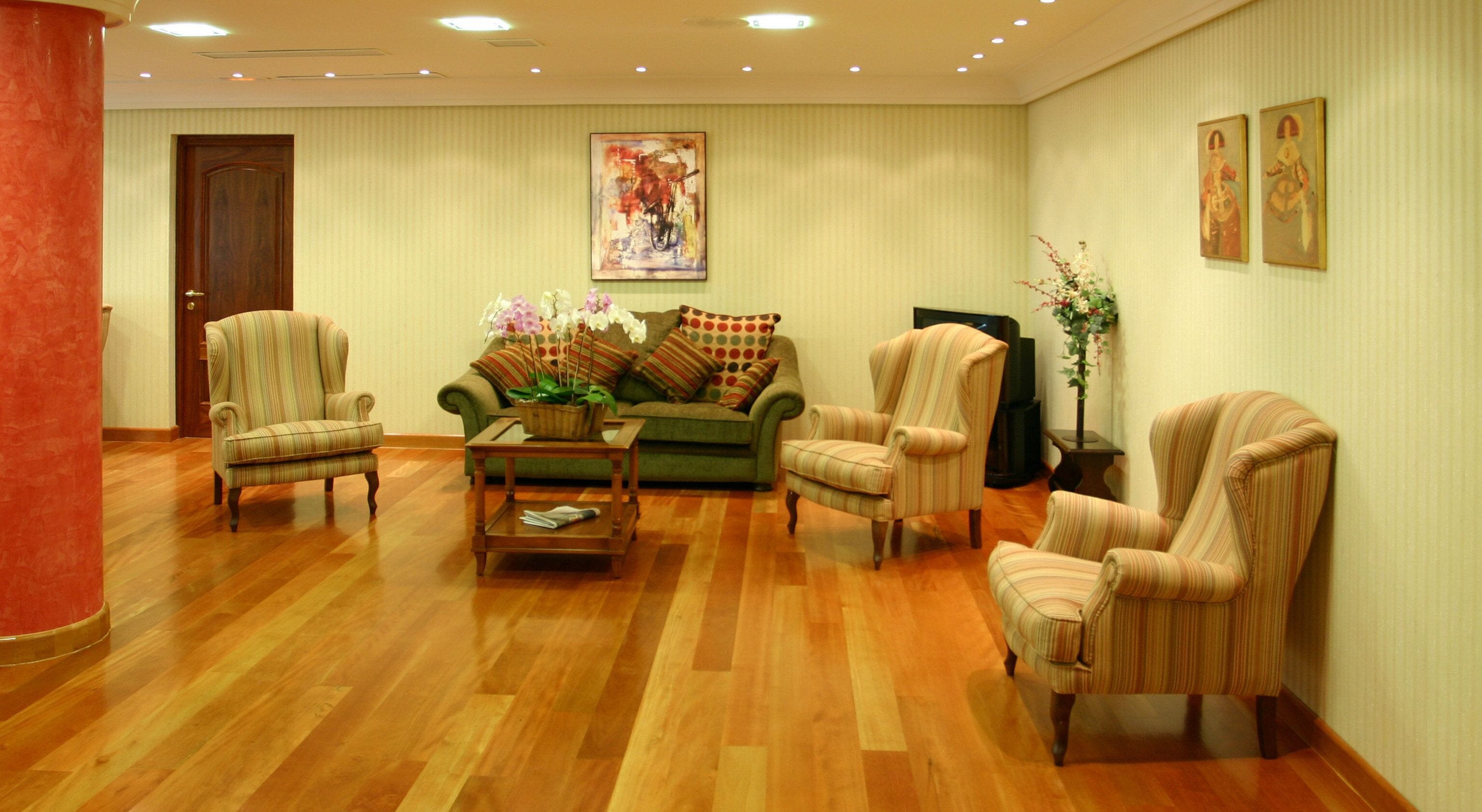 Un salon spacieux avec un plancher en bois, un canapé vert, des fauteuils à rayures et une table basse.