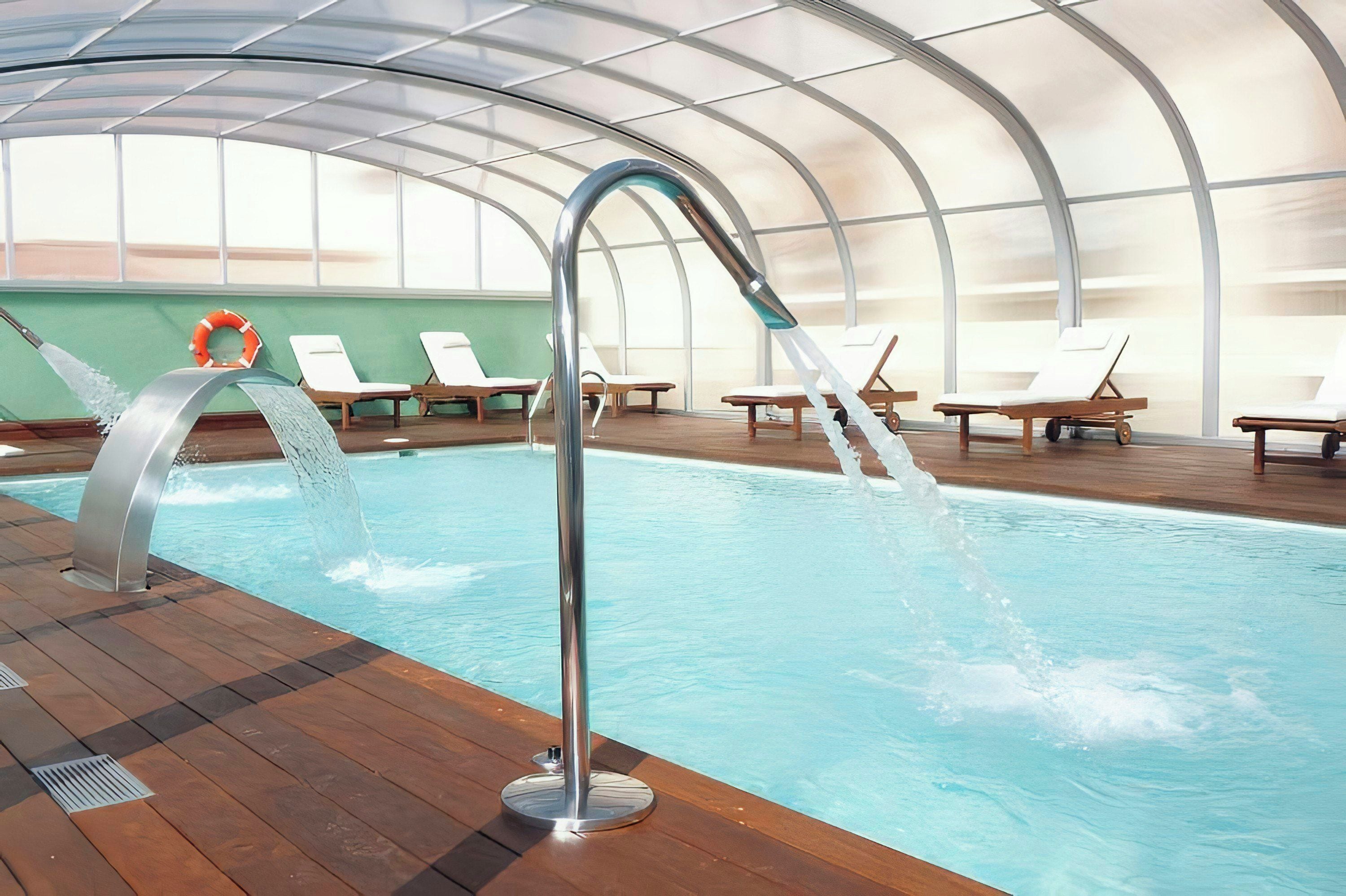 An indoor swimming pool with a modern design, featuring a clear glass ceiling and wooden deck.