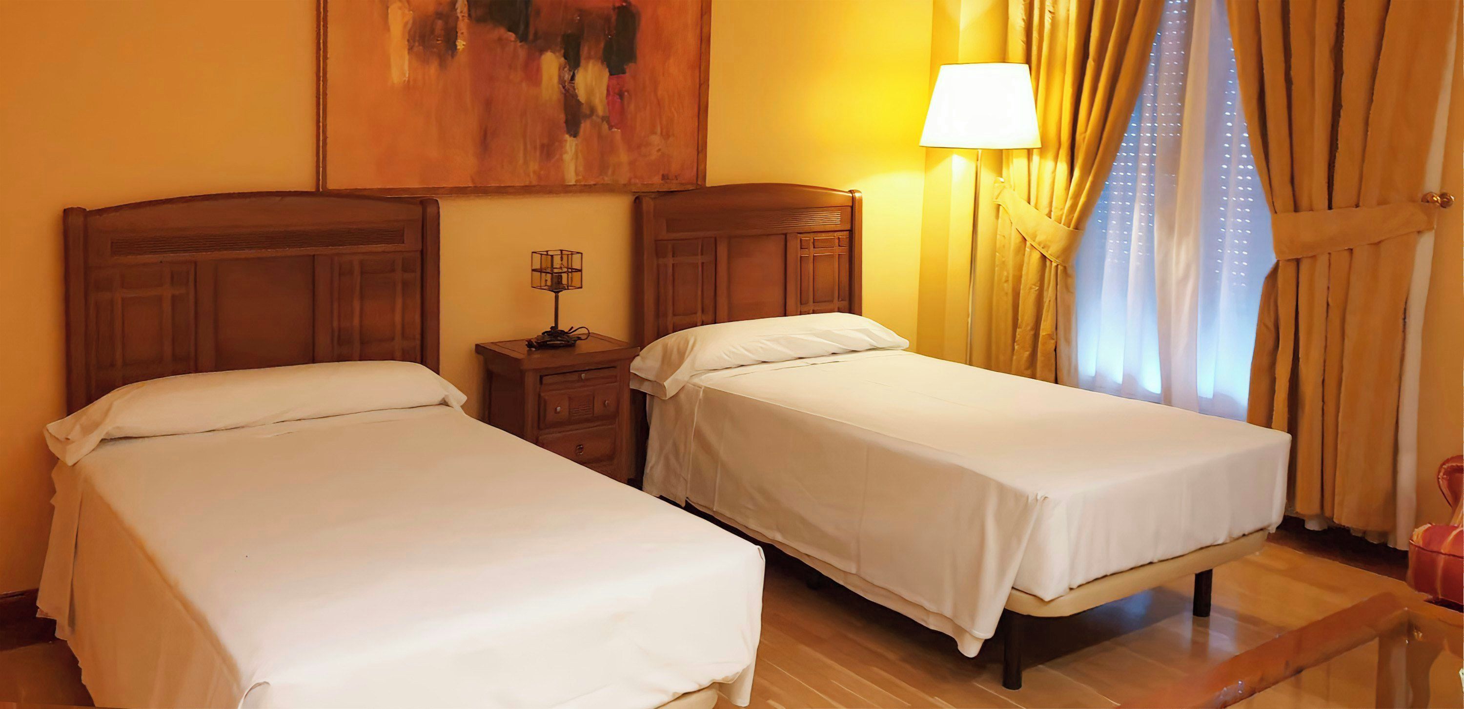 Een hotelkamer met twee enkele bedden, een nachtkastje met een lamp en een schilderij aan de muur.