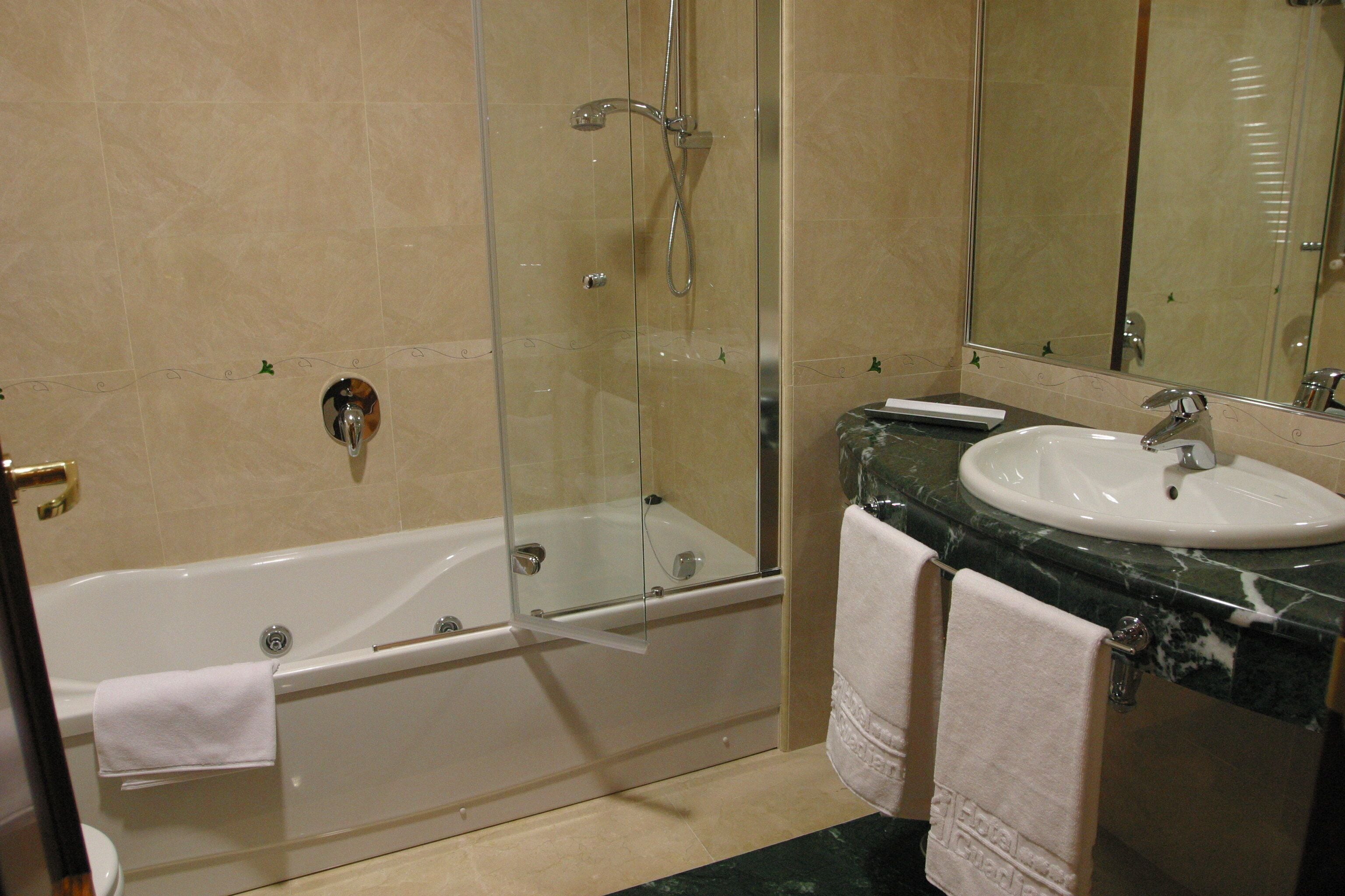 Un baño con ducha de vidrio, una bañera blanca, un lavamanos con encimera de mármol y un espejo grande.