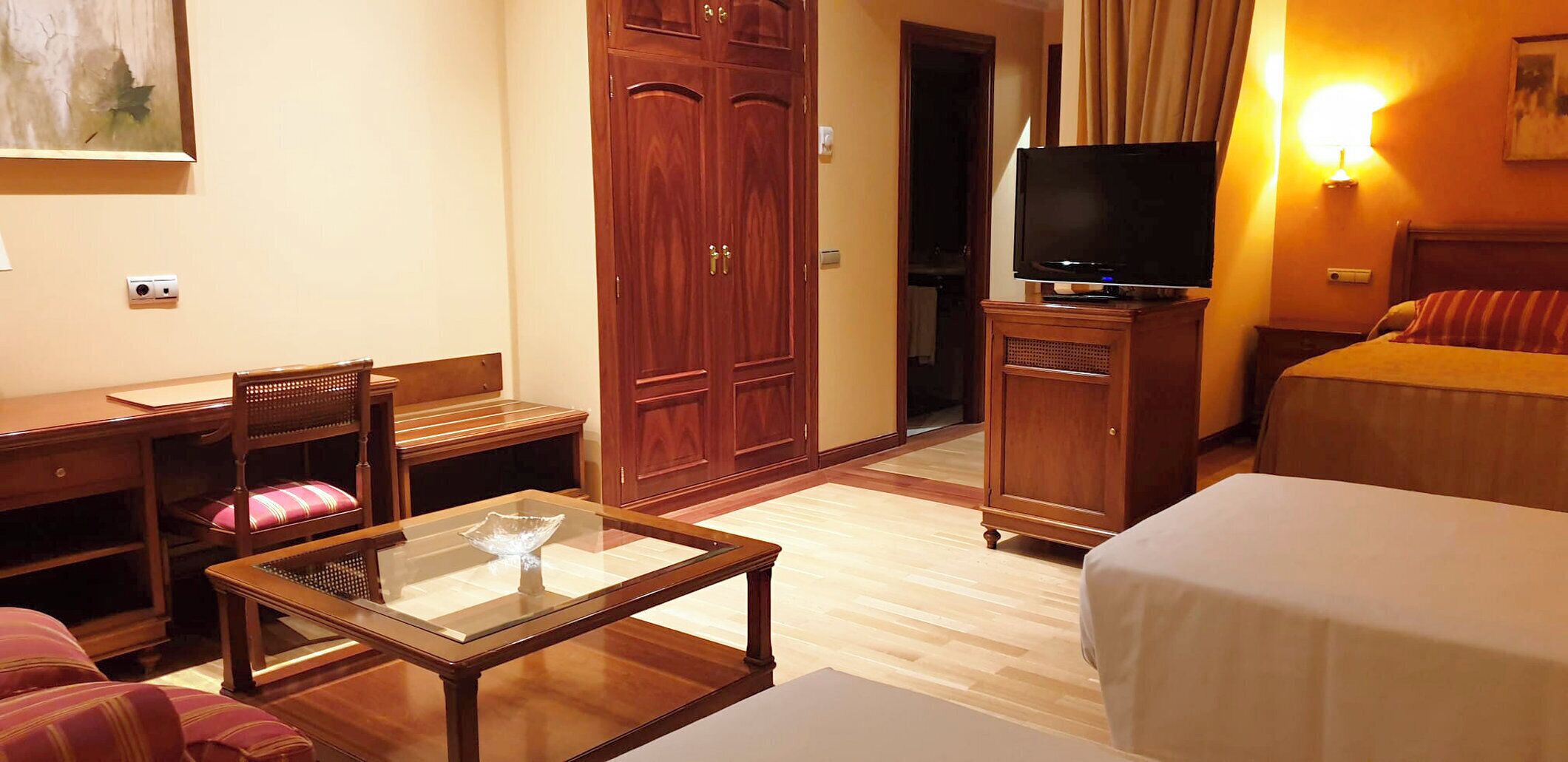 Una habitación de hotel con una cama, un escritorio con silla, un televisor y un armario.