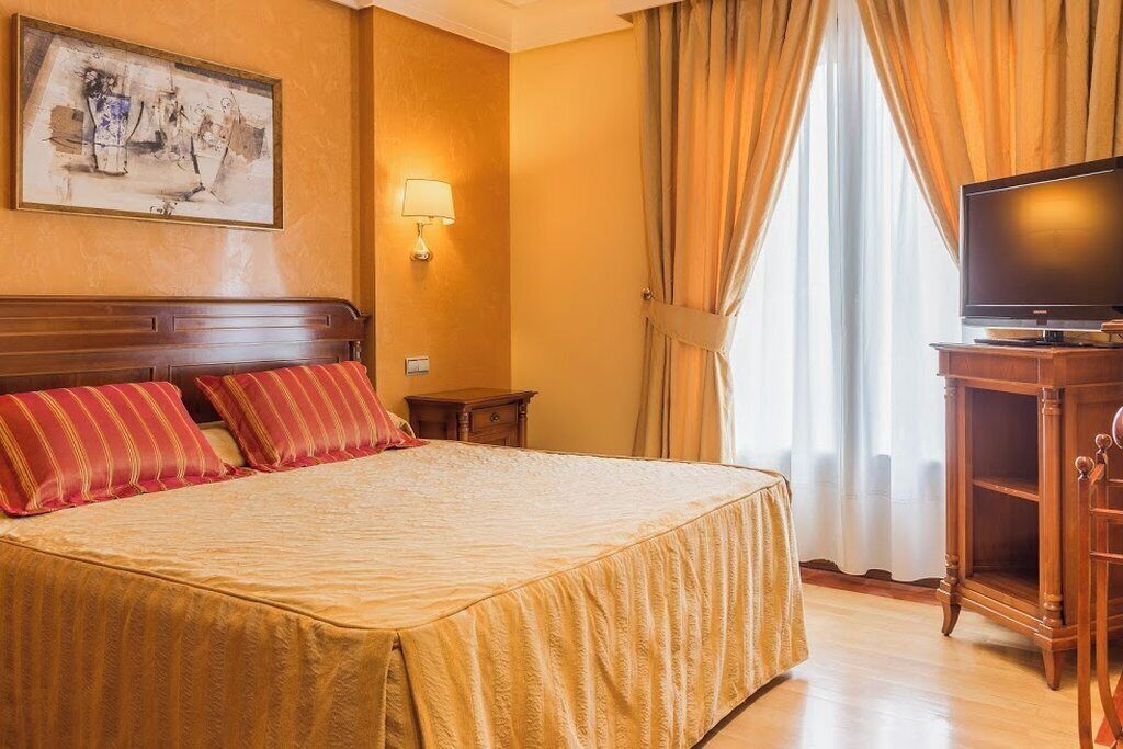 Una habitación de hotel con una cama grande, televisión, mesita de noche y un cuadro en la pared.