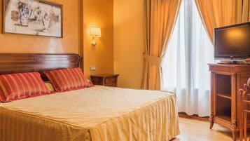 Una habitación de hotel con una cama grande, televisión, mesita de noche y un cuadro en la pared.