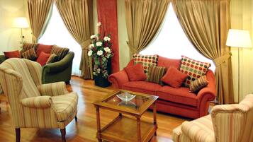 Una sala de estar con sillones a rayas, un sofá rojo con cojines estampados, una mesa de centro de vidrio y un jarrón de flores.