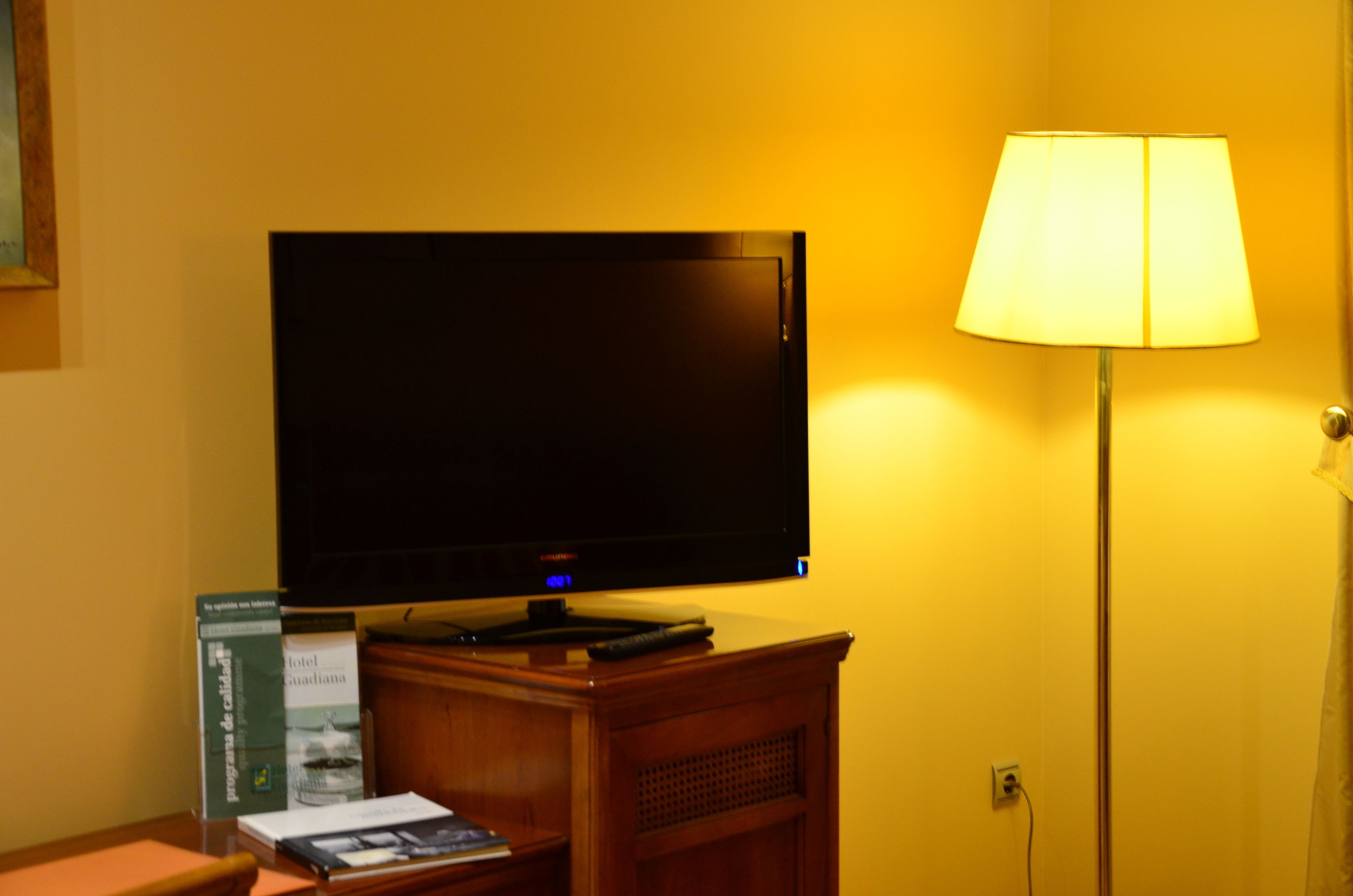 Un televisor sobre un soporte de madera, una lámpara y un libro en una mesa.