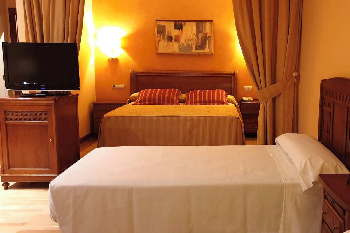 A hotel room with two beds, a television, a bedside table, a lamp, and a painting on the wall.