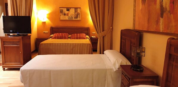 Habitación de hotel con dos camas, un televisor, una mesita de noche, una lámpara y un cuadro en la pared.