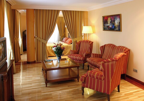 Una habitación de hotel con una cama, dos sillones a rayas, una mesita de centro y un cuadro en la pared.