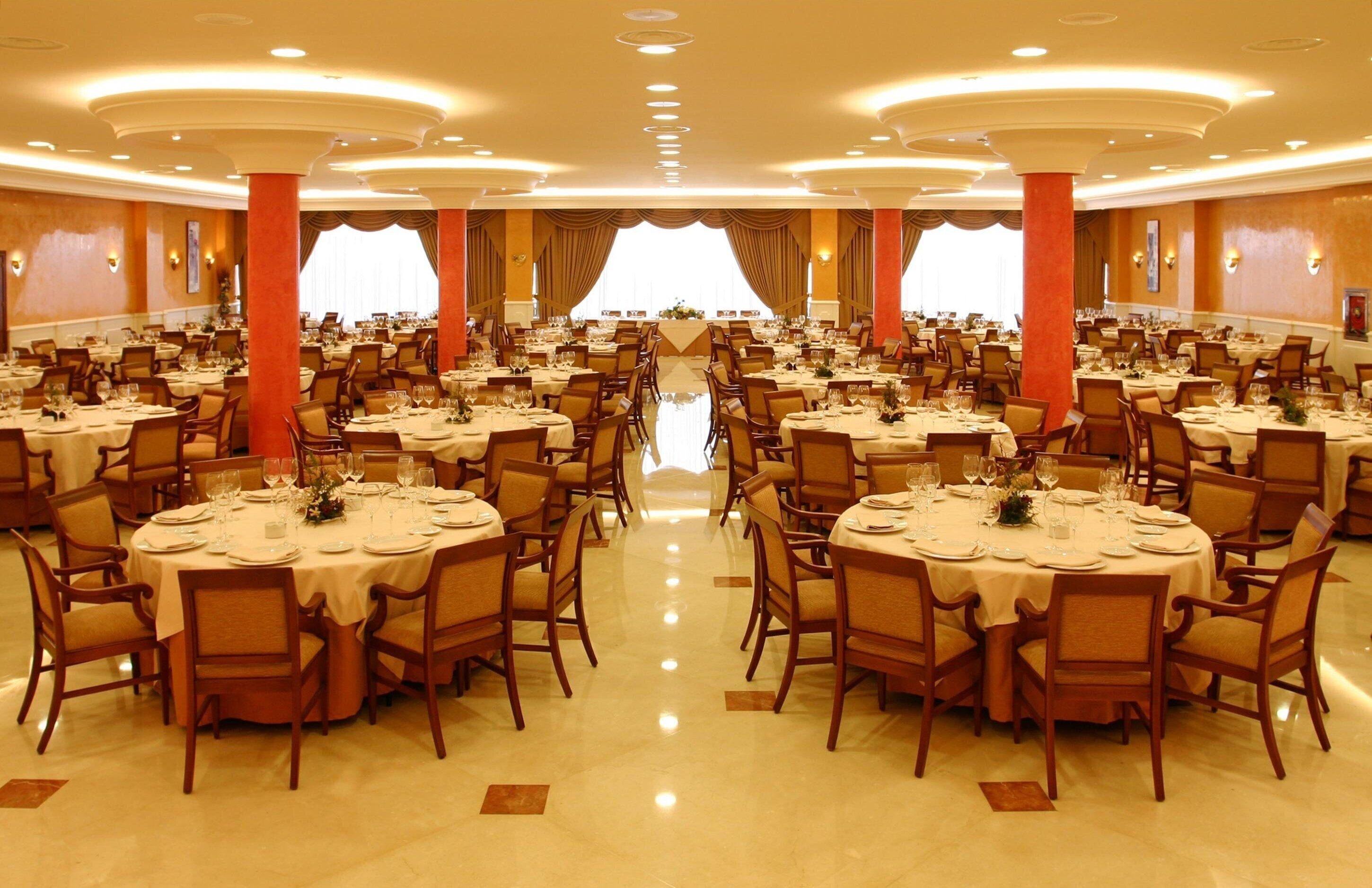 Un amplio salón de banquetes con mesas redondas, sillas y un pasillo central.