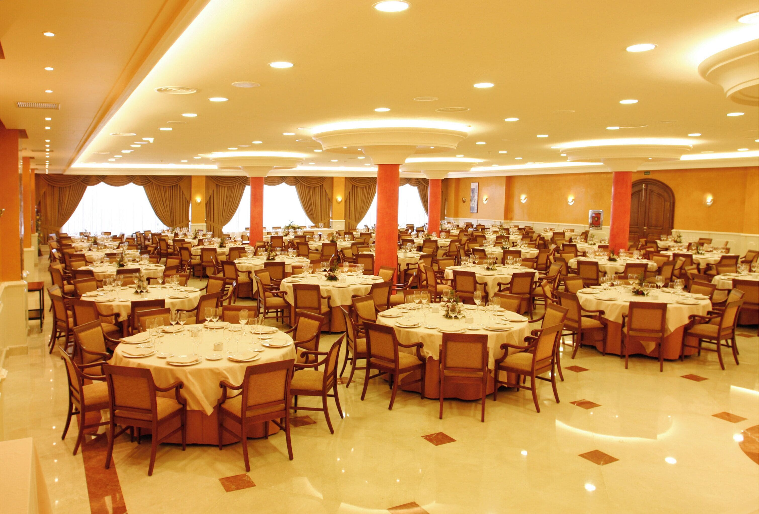 Un amplio salón de banquetes con varias mesas redondas y sillas, dispuestas en filas.