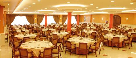 Un amplio salón de banquetes con varias mesas redondas y sillas, dispuestas en filas.
