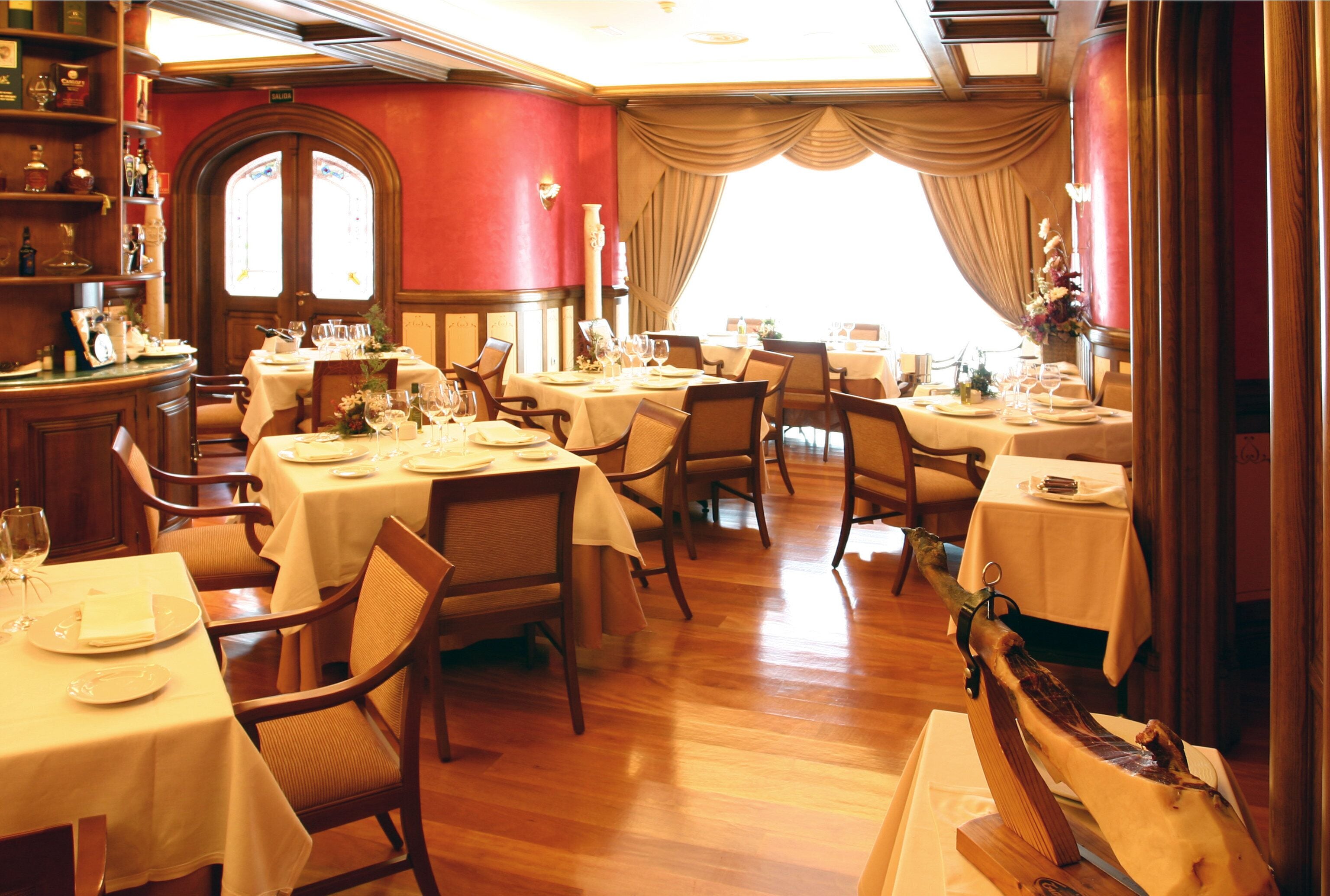 Un restaurante con varias mesas dispuestas para comer, pisos de madera y un amplio ventanal con cortinas.