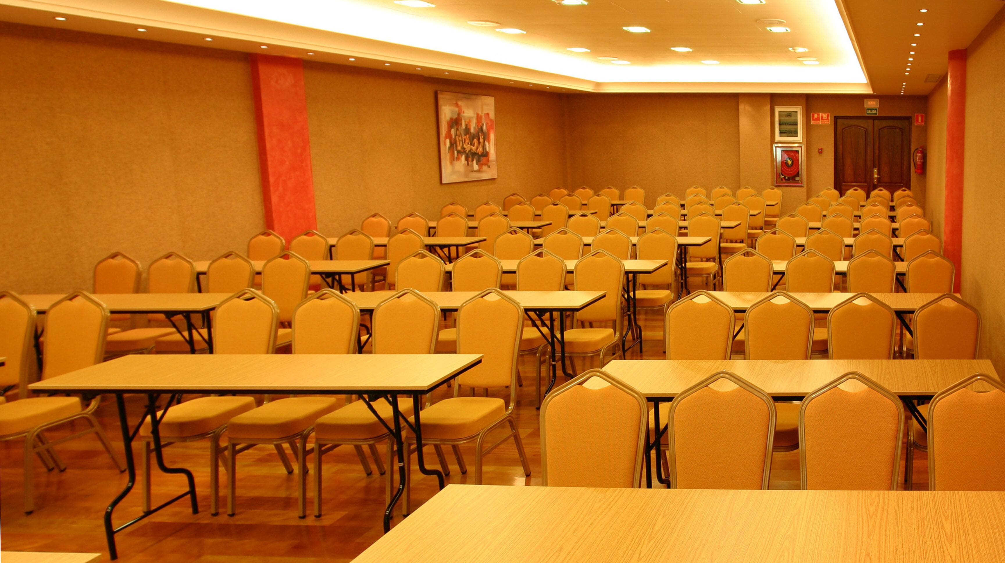 A conference room with rows of tables and chairs, a fire extinguisher, and a door labeled "EXIT".