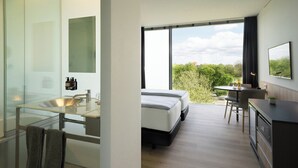 A modern hotel room with a glass shower enclosure, a bed with a view, a dining area, and a kitchen.