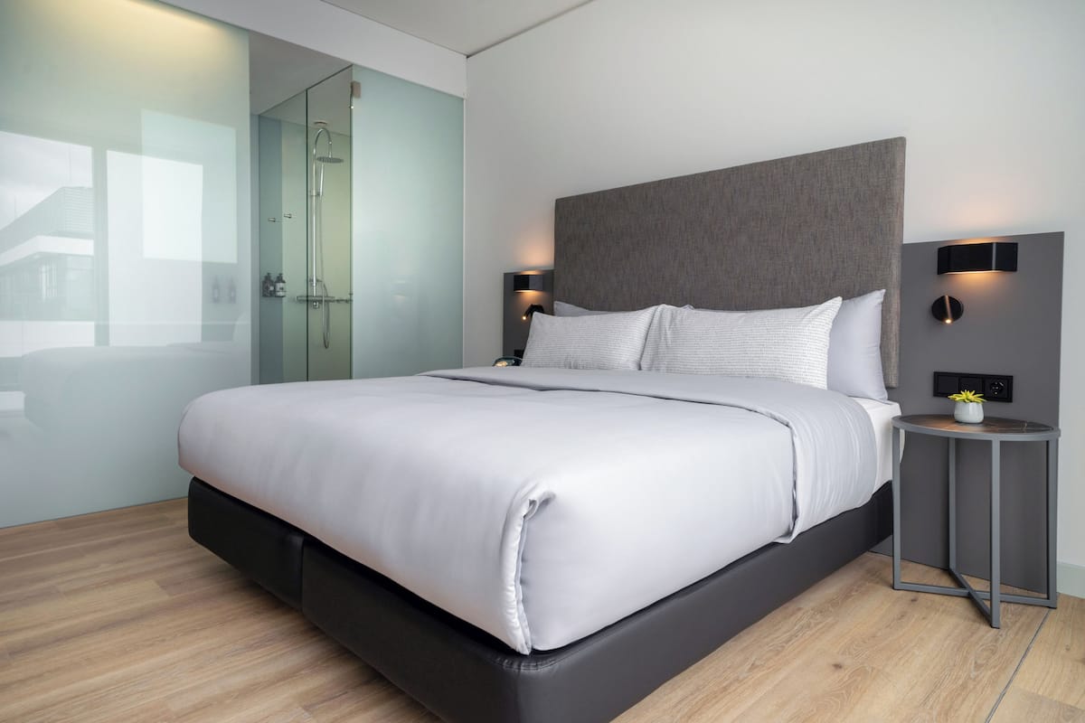 Une chambre à coucher moderne avec un grand lit, des tables de chevet, une cabine de douche en verre et un luminaire fixé au mur.