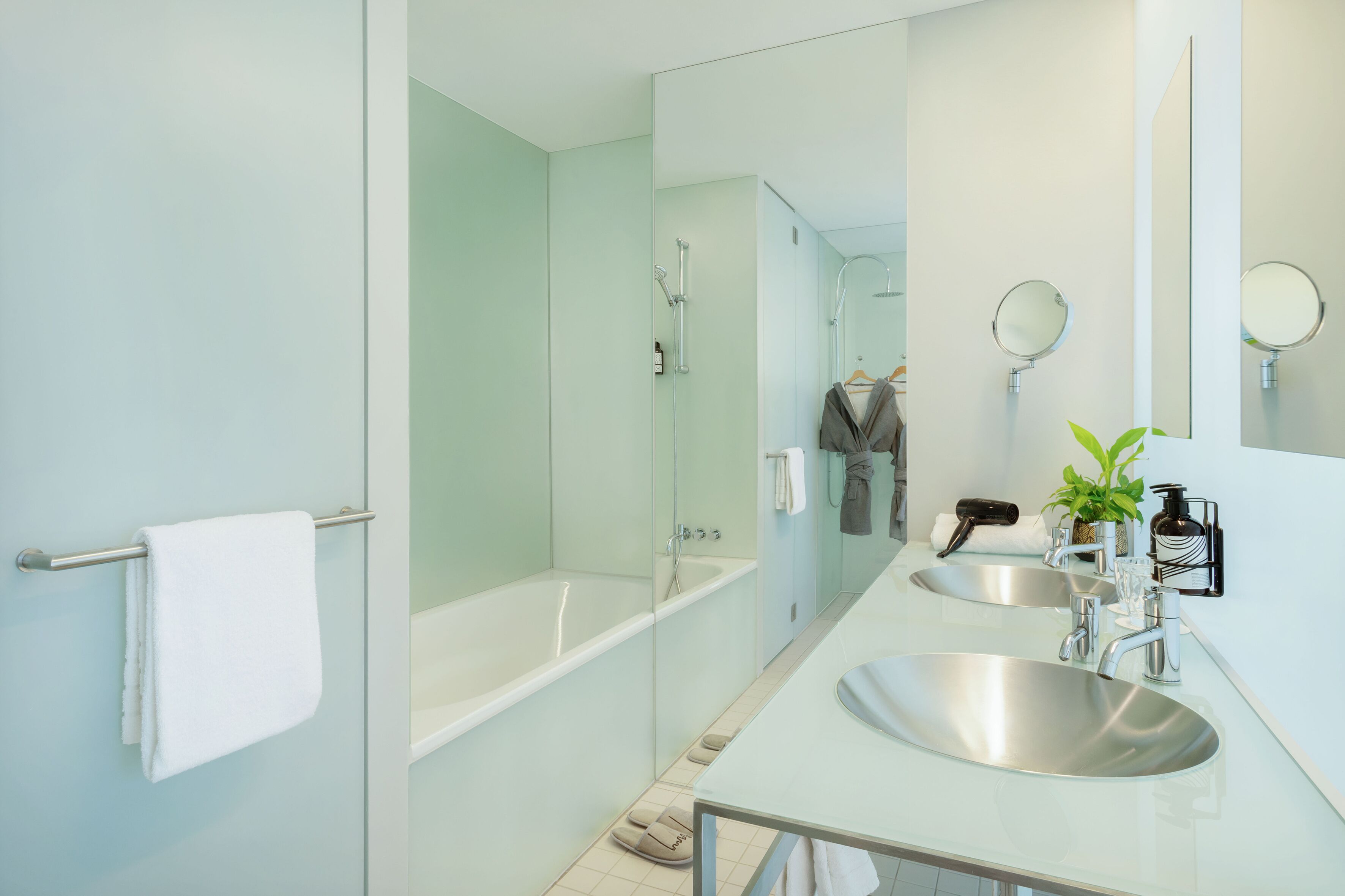 Un baño moderno con ducha de vidrio, dos lavamanos y un espejo grande.