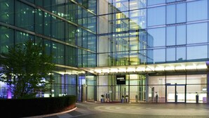 A modern glass building with a reflective facade, a paved entrance area, and a sign reading "INSIDE."