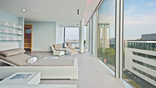 A modern hotel room with a balcony, large windows, and a view of the city.