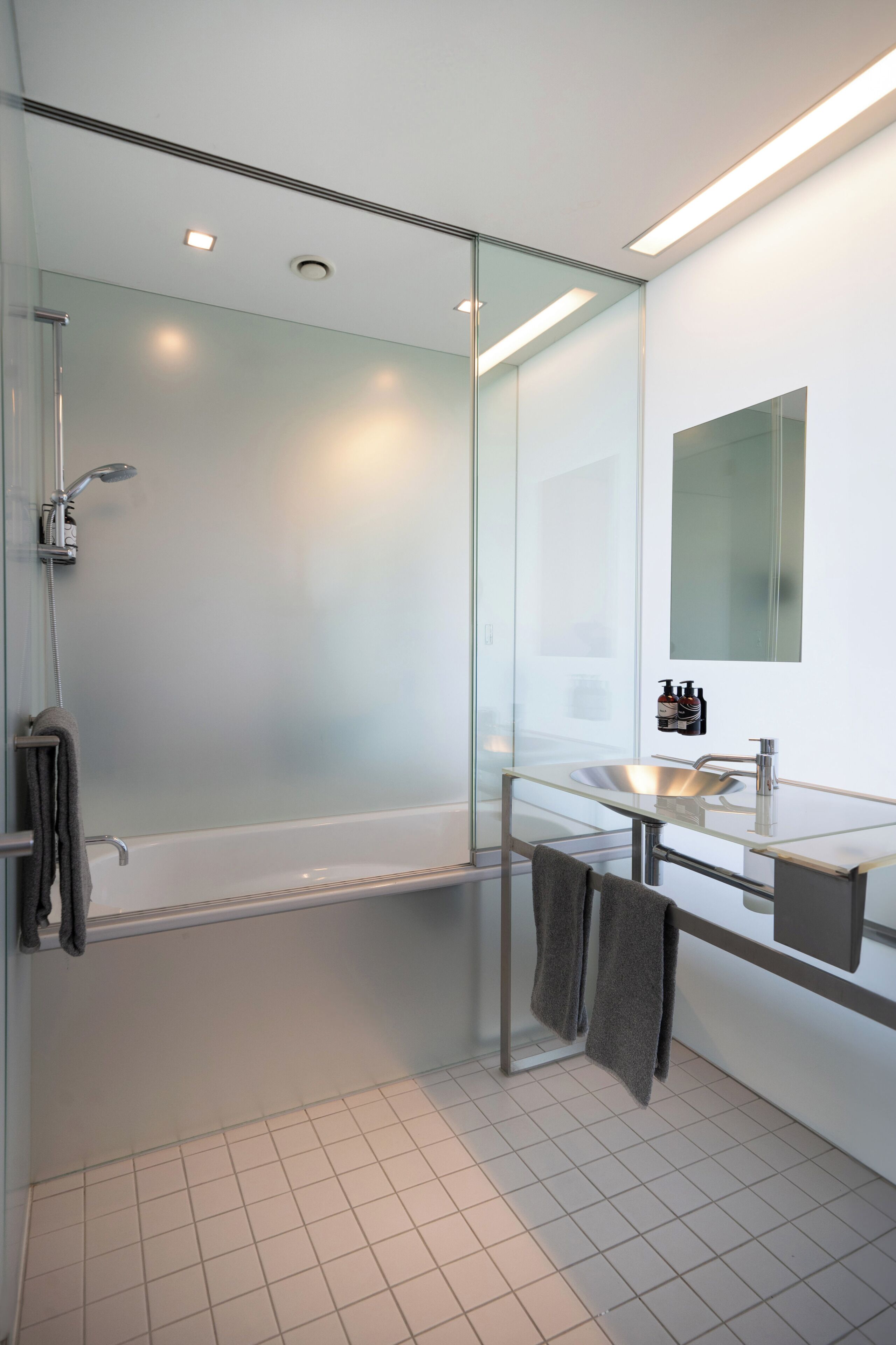 Een moderne badkamer met een douchecabine van glas, een wastafel met glazen blad en een grote spiegel.
