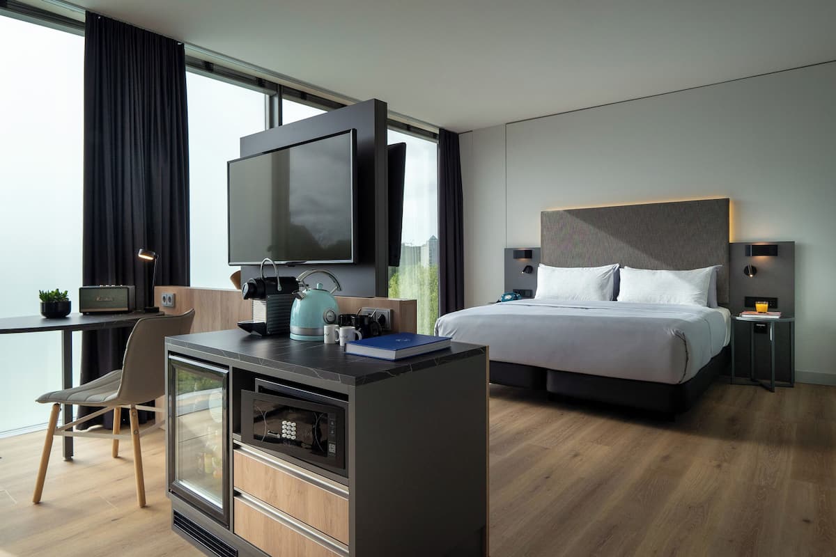 Une chambre d’hôtel moderne dotée d’un grand lit, d’un bureau avec une télévision, d’une machine à café et offrant une vue sur la ville.