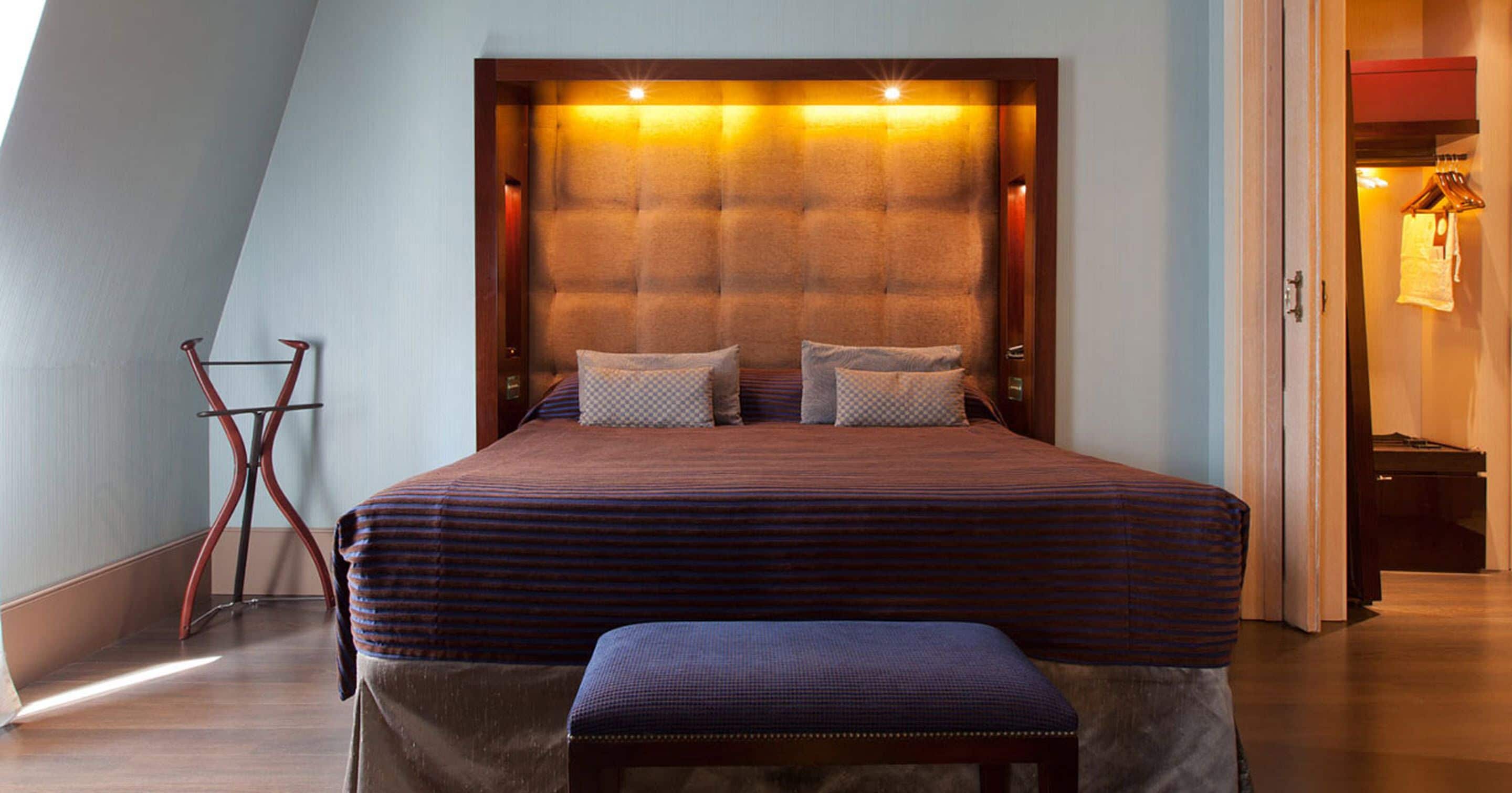 Un dormitorio con una cama grande, un banco y un cabecero con iluminación integrada.