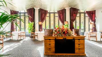 Une pièce avec un bureau en bois, deux lampes, une grande fenêtre avec des rideaux et une plante en pot.