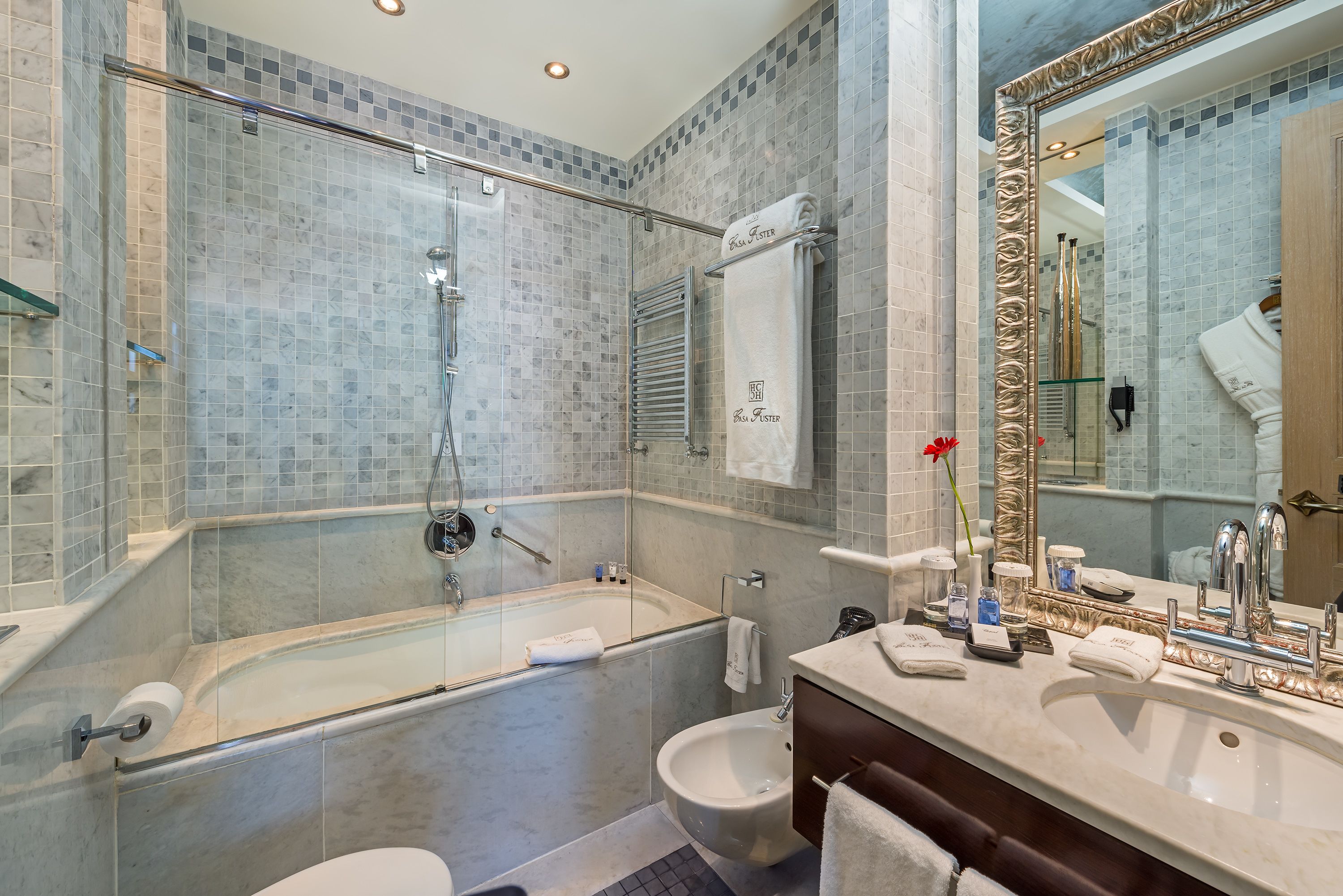 A modern bathroom with a glass-enclosed shower, a freestanding bathtub, a bidet, and a vanity with a large mirror.