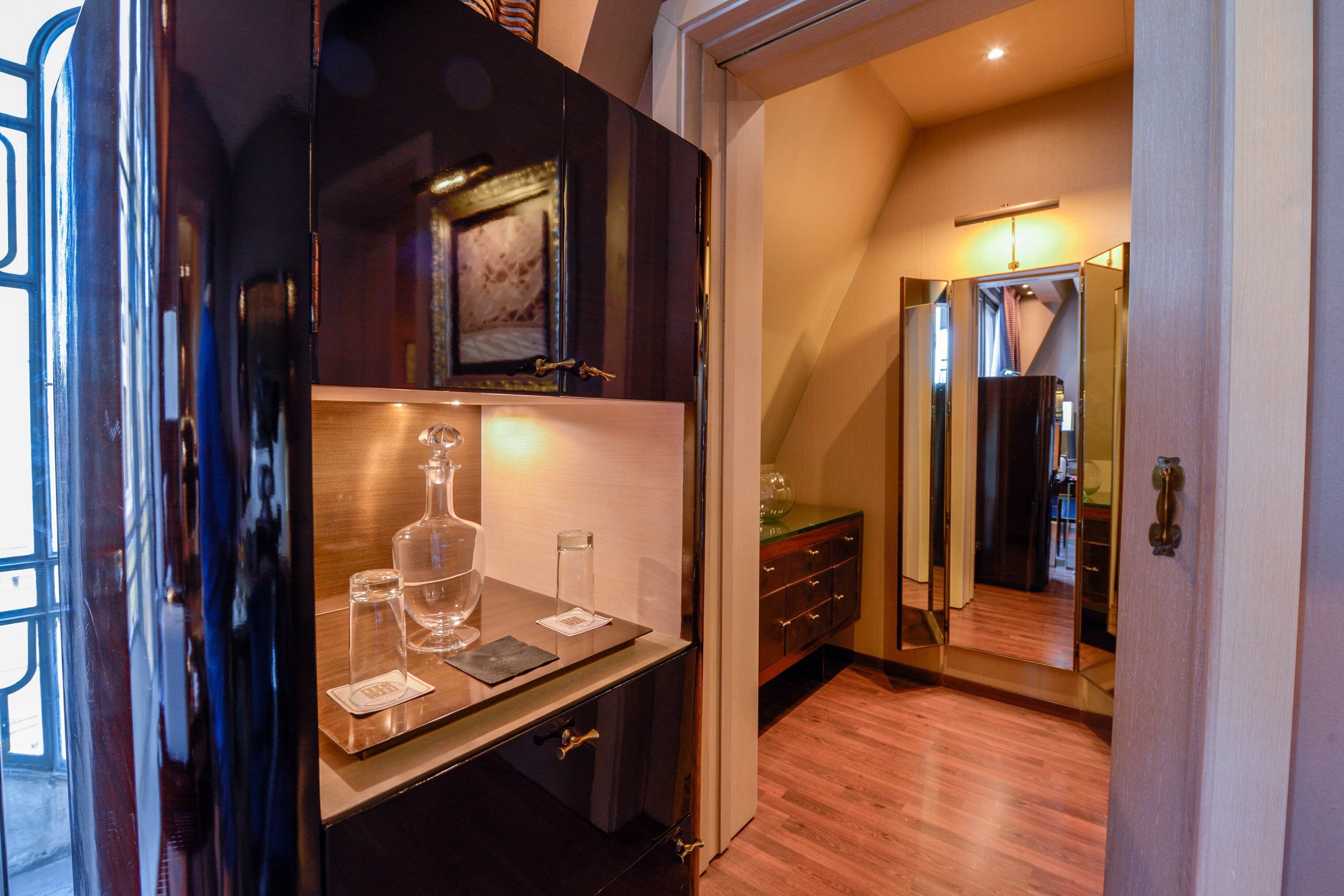 A hotel room with a wooden floor, a minibar, and a mirror reflecting the room.