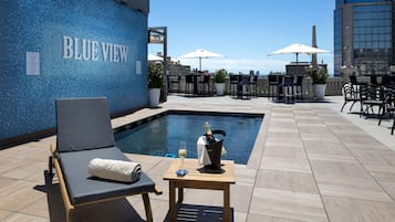 Uma área de piscina no terraço com uma espreguiçadeira, uma mesa com uma garrafa de champanhe e guarda-sóis.