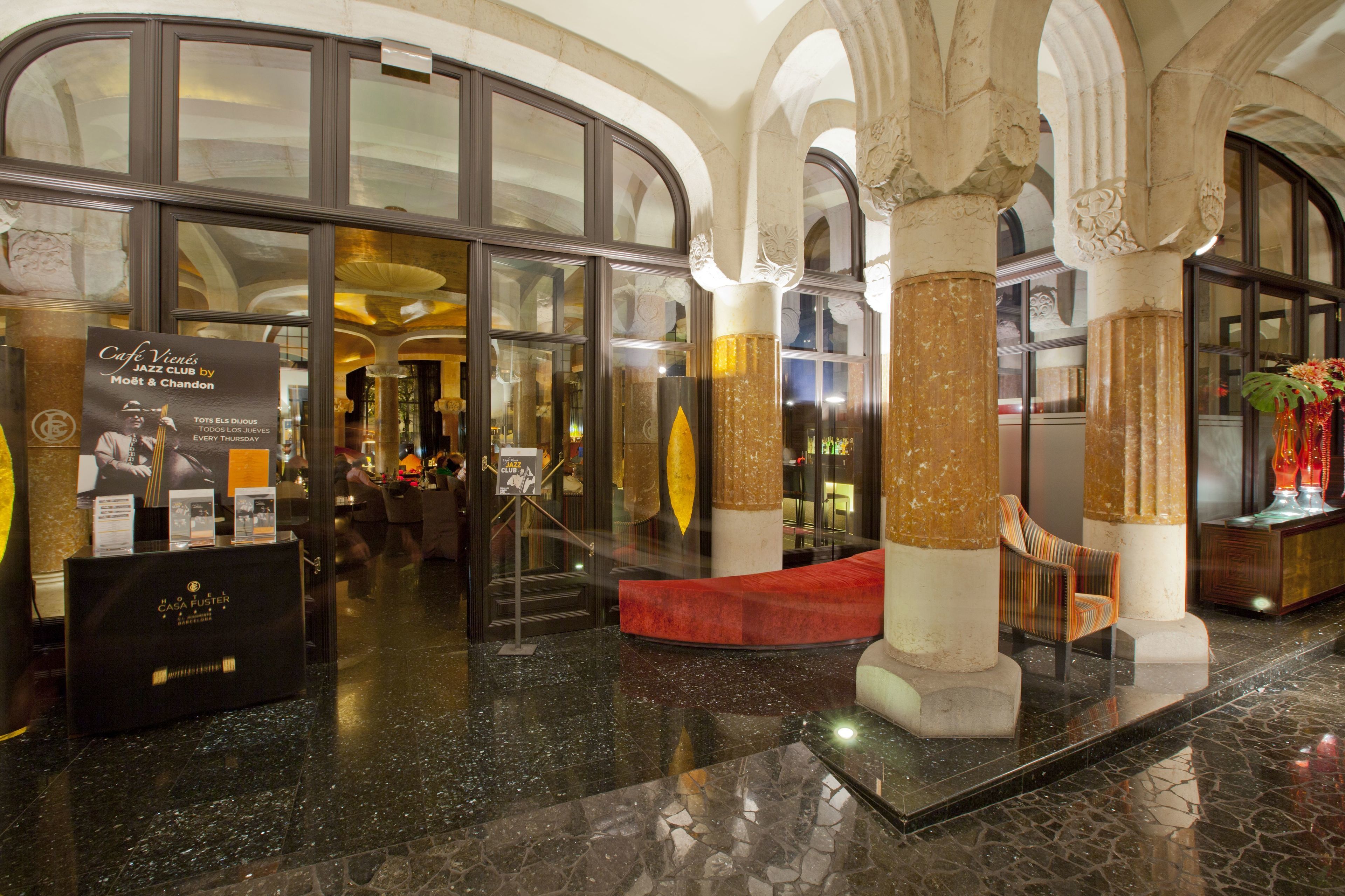 A lobby with a glass entrance, marble flooring, and a red seating area.