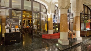 A lobby with a glass entrance, marble flooring, and a red seating area.