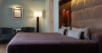 Habitación de hotel con una cama grande, un escritorio, una silla, una lámpara y un cuadro en la pared.