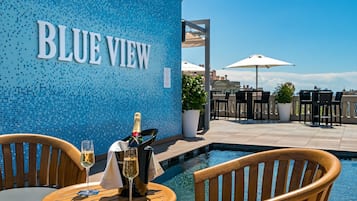 A poolside area with a "BLUE VIEW" sign, outdoor seating, and a bottle of champagne.