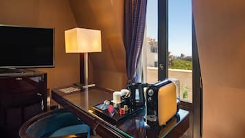Hotelkamer met een bureau, een lamp, een koffiezetapparaat en uitzicht op groen.
