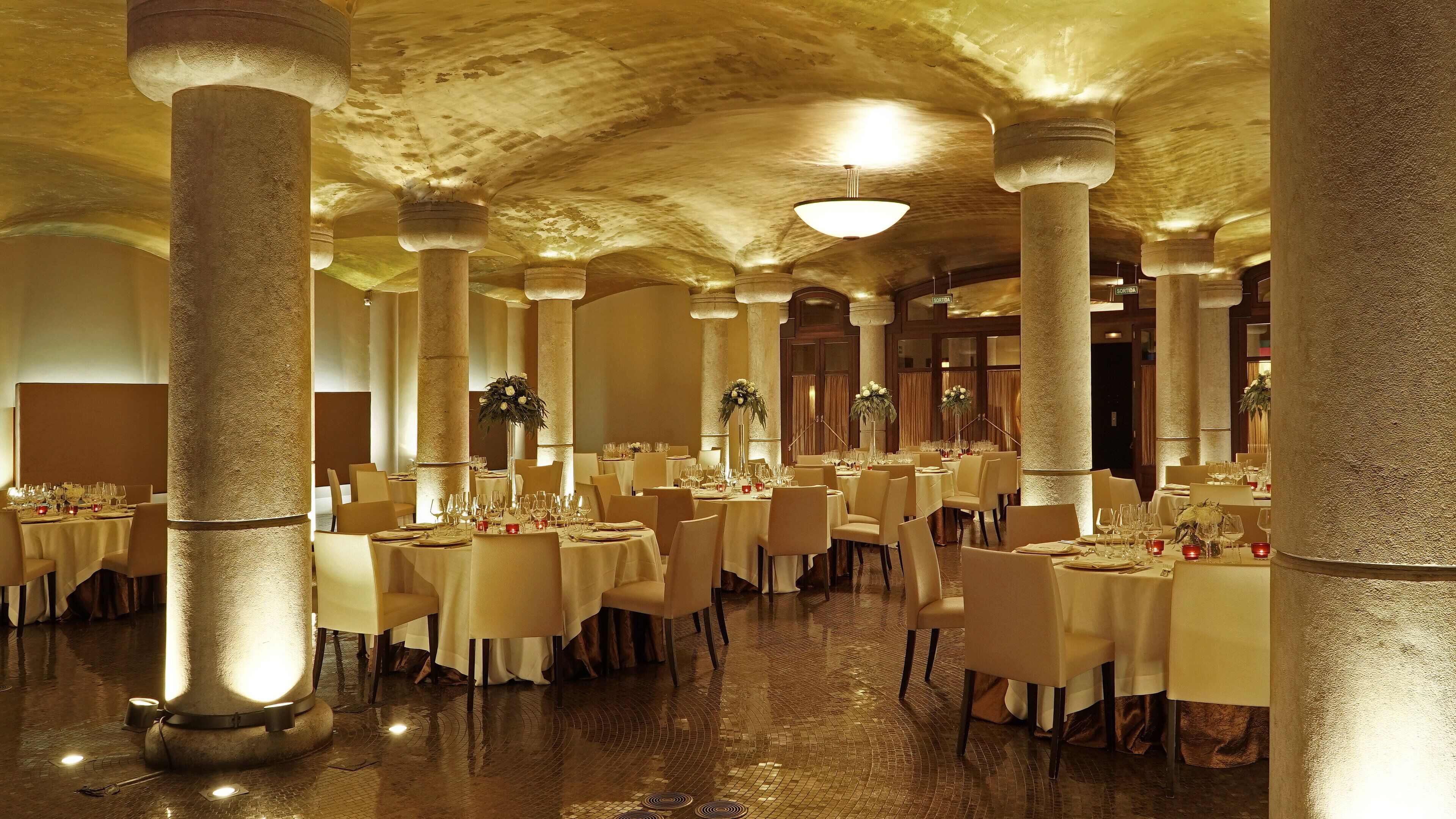 A spacious banquet hall with high ceilings, large stone columns, and round tables set for dining.