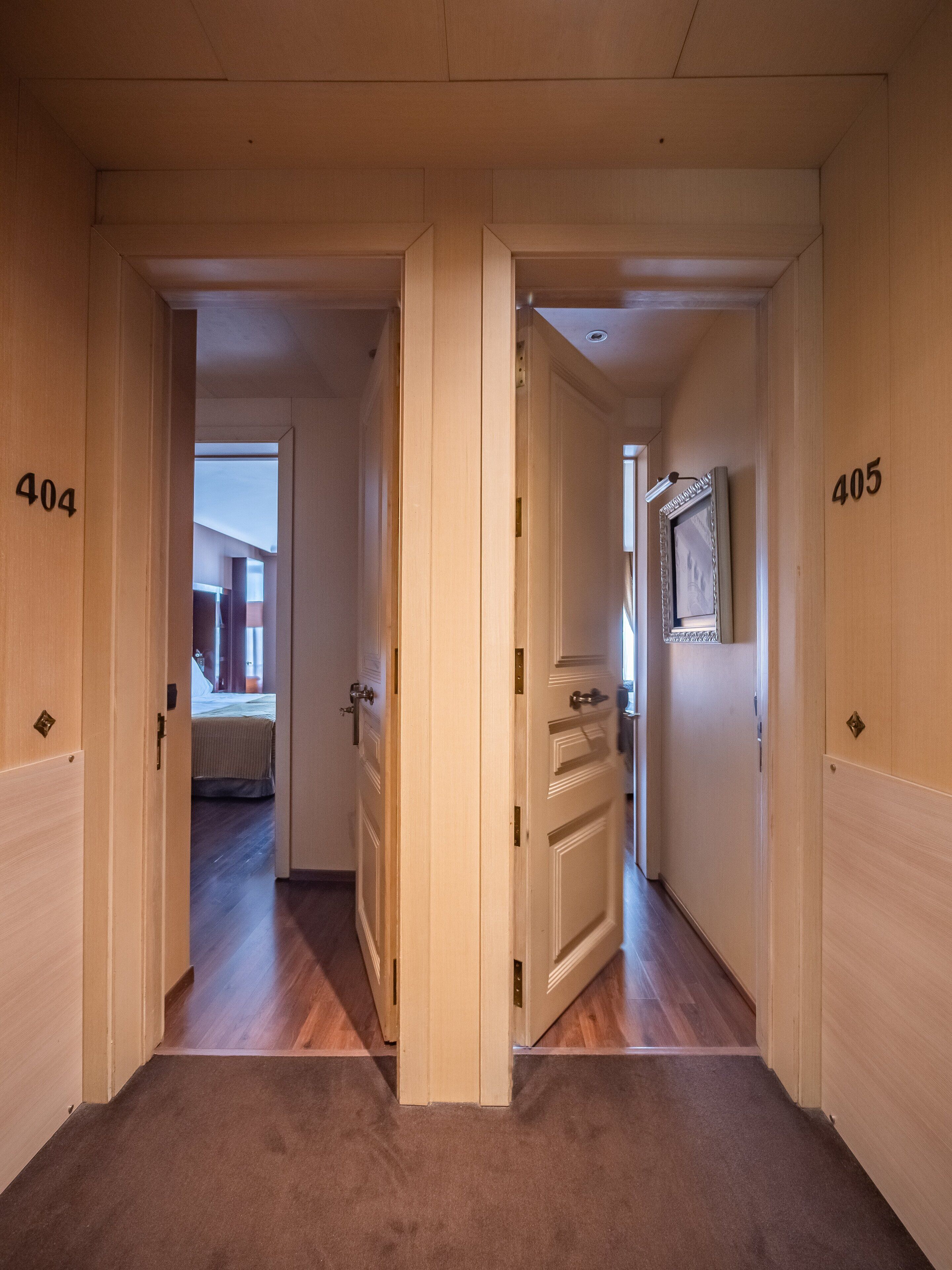 A hallway with wooden doors numbered 404 and 405, leading to a bedroom with a bed and a bathroom with a mirror and framed picture.