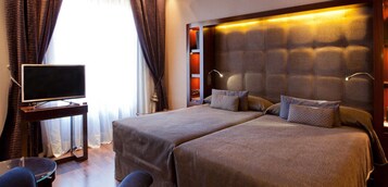 A hotel room with a large bed, a TV on a stand, and a window with curtains.