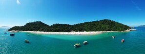 A tropical island with a white sandy beach, clear turquoise waters, and several boats. - Morro das Pedras Clube Hotel (Florianópolis)