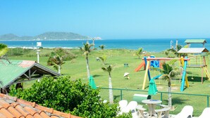 A beach view with a playground and a fenced area with tables and chairs. - Morro das Pedras Clube Hotel (Florianópolis)