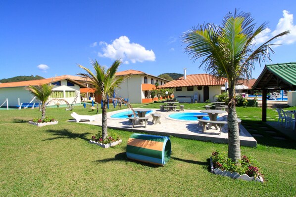 Un área de piscina con sillones de descanso, una piscina pequeña y palmeras.