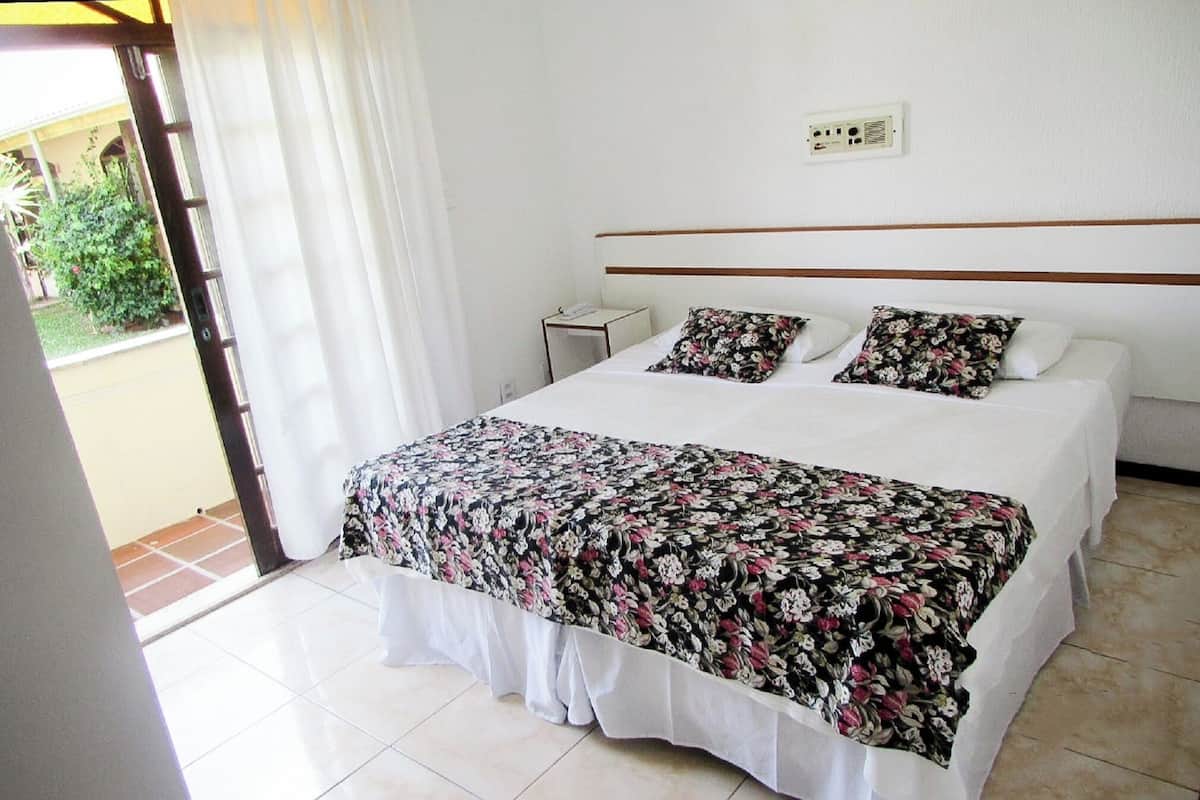 A hotel room with a bed, a nightstand, and a view of the outside.
