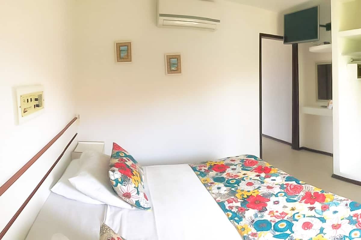 A bedroom with a bed, a wardrobe, and a bathroom visible in the background.